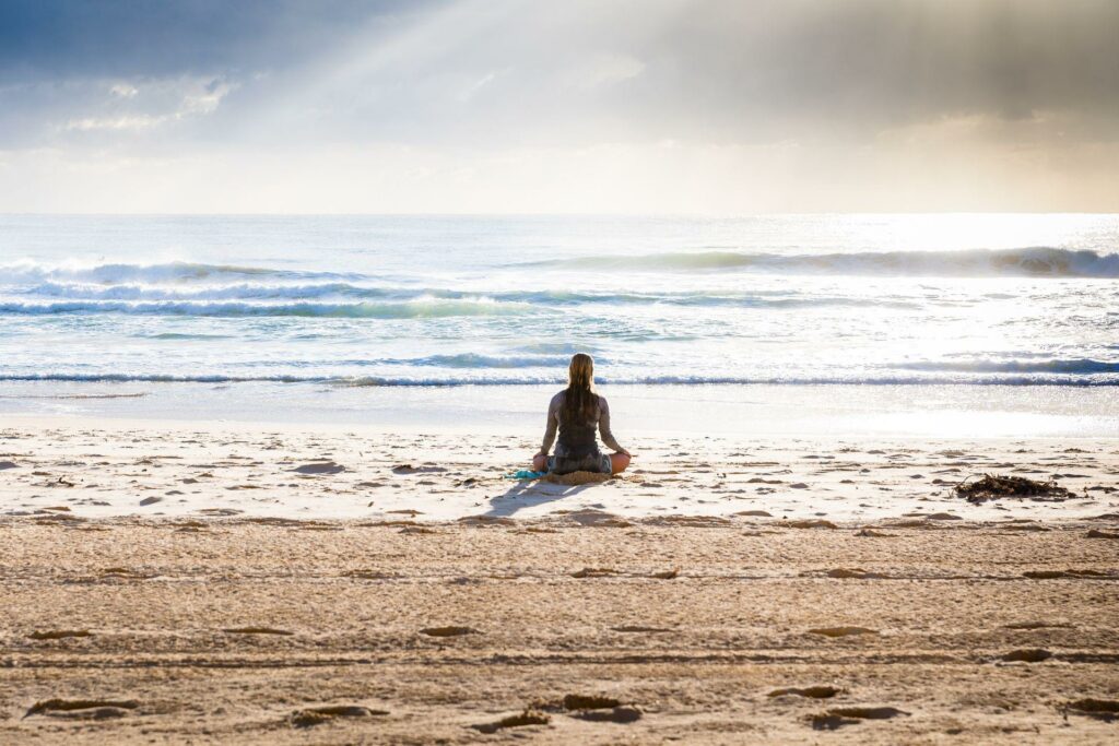 En kvinde sidder og laver meditation og mindfulness på en strand